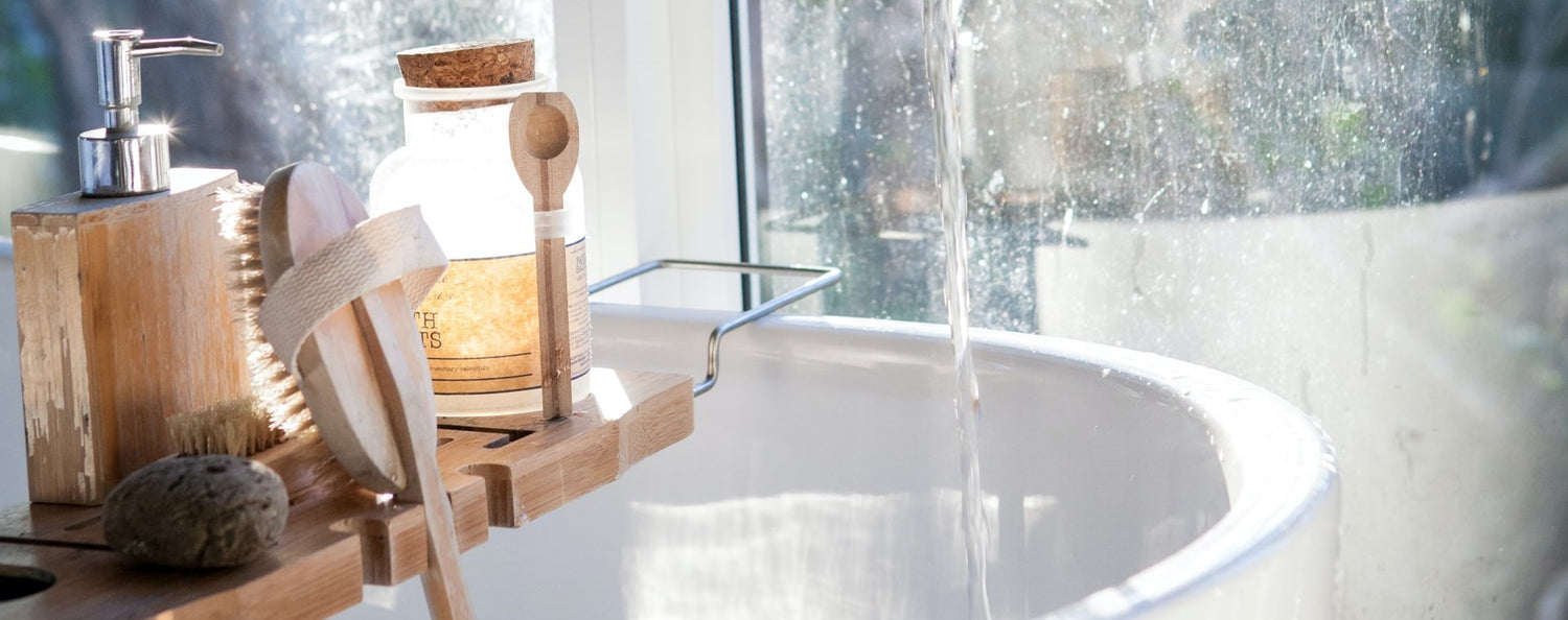 Water pours into a white bathtub, next to a tray of various bath salts, soaps, and accessories.