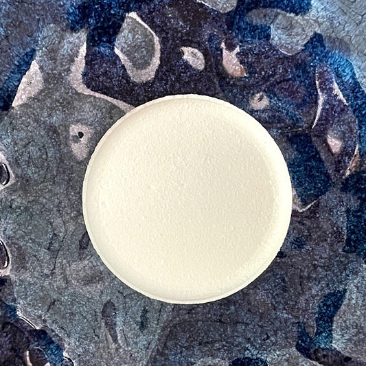 A solid white puck of compressed powder resting on a textured blue ceramic surface.